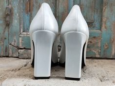 a pair of white high heeled shoes sitting on top of a wooden floor next to an old door