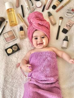 a baby laying on top of a towel next to makeup and other cosmetics items in the background