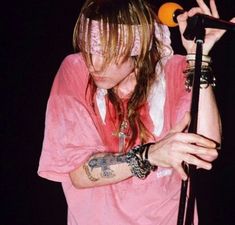 a man with long hair and piercings on his arm holding a microphone in front of him