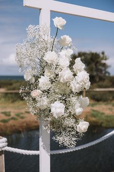 a bouquet of white flowers sitting on top of a wooden cross next to a body of water