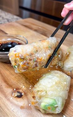 someone holding chopsticks over some food on a cutting board with dipping sauce in the background