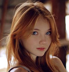 a young woman with red hair and blue eyes posing for a photo in front of a window