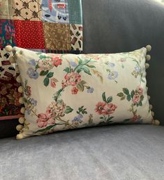 a floral pillow with pom poms on it sitting next to a gray couch