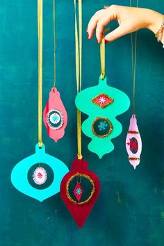 three handmade ornaments hanging from strings against a blue wall with green paint on it