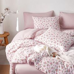 an unmade bed with pink sheets and flowers on it, next to a wooden table