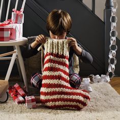 a young boy sitting on the floor with presents in front of him and wrapping them up