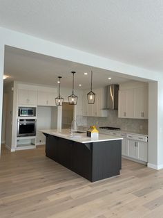 an empty kitchen with white cabinets and black island in the center is lit by pendant lights