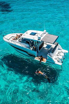 a man swimming in the ocean next to a small white boat with people on it