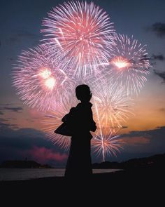 a person standing in front of a firework display at night with the sun setting