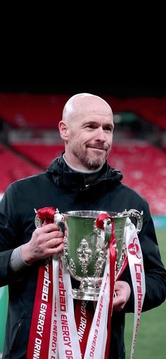 a man holding a silver trophy on top of a field with red and white ribbons