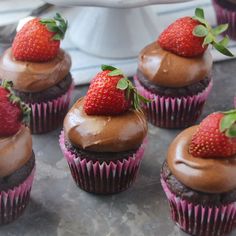 cupcakes with chocolate frosting and strawberries on top are sitting on a table