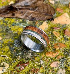 a wedding band with wood inlays sits on top of green moss and leaves