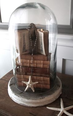 a glass dome with books under it on top of a wooden table next to starfish