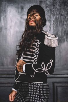 a man with long hair wearing a black and white uniform standing in front of a wall