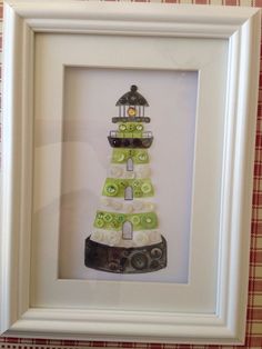 a white frame with a green and white lighthouse made out of buttons in the shape of a light house