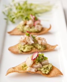 three appetizers are arranged on a white plate with green garnishes