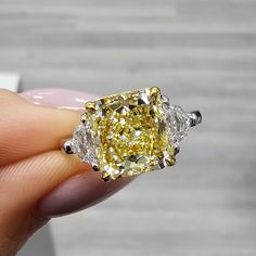 a fancy yellow diamond ring being held in someone's hand