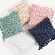 four different colored pillows with tassels on the sides and one is white, pink, blue, green