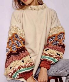 a woman sitting on top of a wooden chair wearing a white sweater with multicolored stripes