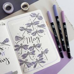 an open notebook with dragonflys on it next to some markers and pencils