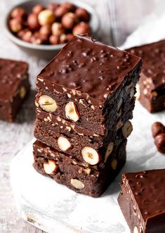 three pieces of chocolate brownie stacked on top of each other with nuts in the background