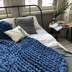 a bed with a blue blanket on top of it next to a table and window