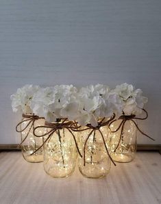 white flowers are in mason jars with string lights