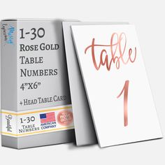 the rose gold table numbers are on display in front of a white box with pink foil lettering