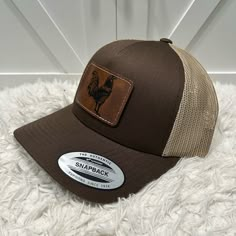 a brown and tan trucker hat sitting on top of a white fluffy rug with a chicken patch