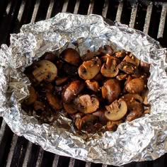 mushrooms and other vegetables are cooking on an outdoor grilling pan with tin foil over it