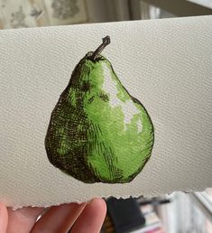 a hand holding up a piece of paper with a drawing of a pear on it