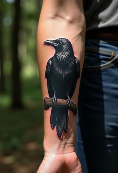 a black bird sitting on top of a tree branch in front of someone's arm