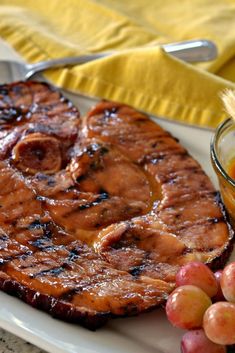 a grilled steak and grapes on a white plate next to a glass bowl of fruit