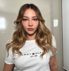 a woman with long hair standing in front of a white wall wearing a tommy hilfiger t - shirt