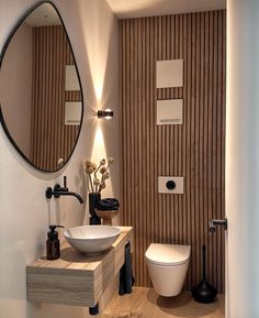 a white toilet sitting next to a bathroom sink under a round mirror on a wall