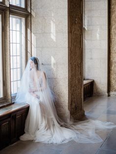 a woman in a wedding dress sitting on a bench next to a window with sunlight streaming through the windows