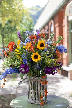 a basket filled with lots of colorful flowers on top of a table next to a building