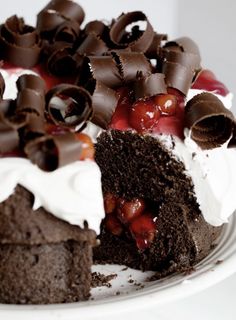 a piece of chocolate cake with whipped cream and cherries on top, sitting on a white plate