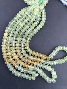 green and yellow glass beads with tassels on a black surface, next to a string of other beads