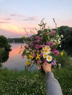 a person is holding a bouquet of flowers by the water at sunset or dawn with pink, yellow and white flowers