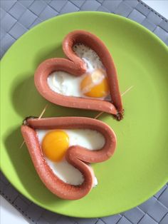 two sausages with eggs in the shape of hearts on a green plate