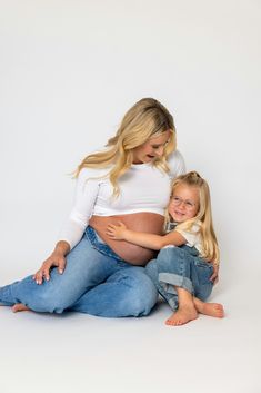 a pregnant woman and her daughter sitting on the floor in front of a white background