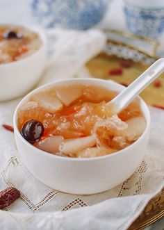 two bowls filled with food on top of a white table cloth next to cups and saucers