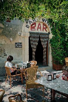 two people sitting at a table in front of a building with vines growing on it