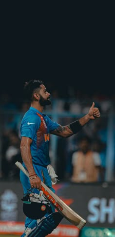 a man with a beard holding a cricket bat and giving the thumbs up while standing on a field