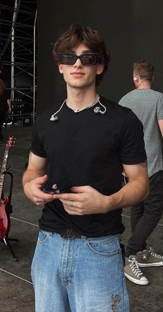 a young man wearing sunglasses standing in front of a guitar and holding his hands together