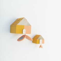 two wooden houses are hanging from hooks on the wall, one is yellow and the other is pink