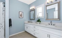 a bathroom with blue walls and white cabinets, two mirrors on the wall above the sinks