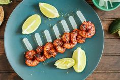 a blue plate topped with grilled shrimp and lemon wedges next to lime slices