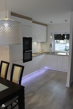 a modern kitchen with white cabinets and wood flooring is lit up by an overhead pendant light